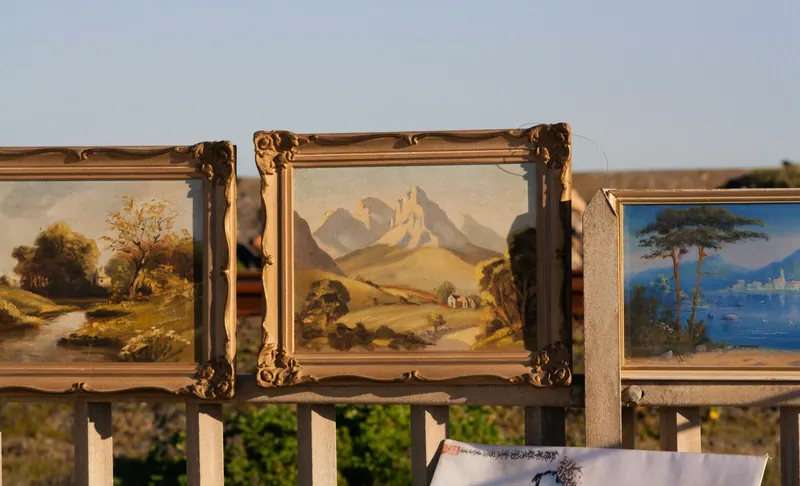 Three landscape paintings in gold frames on a railing