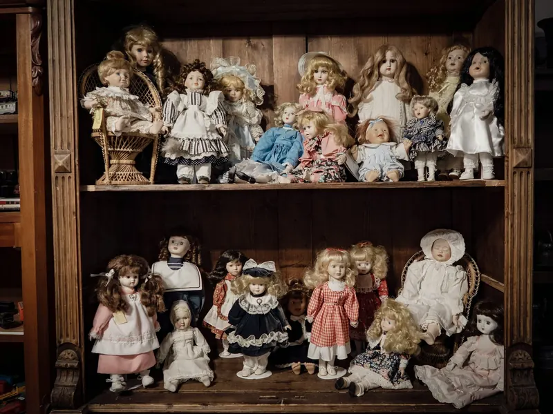 Antique dolls in dresses on two wooden shelves of a cabinet
