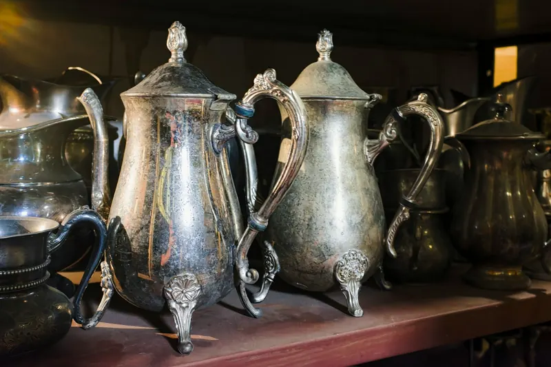 Two old silver jugs with feet on a shelf